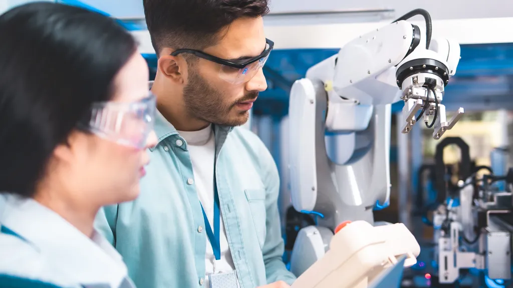 Two researchers examining a robotic arm in a laboratory setting.