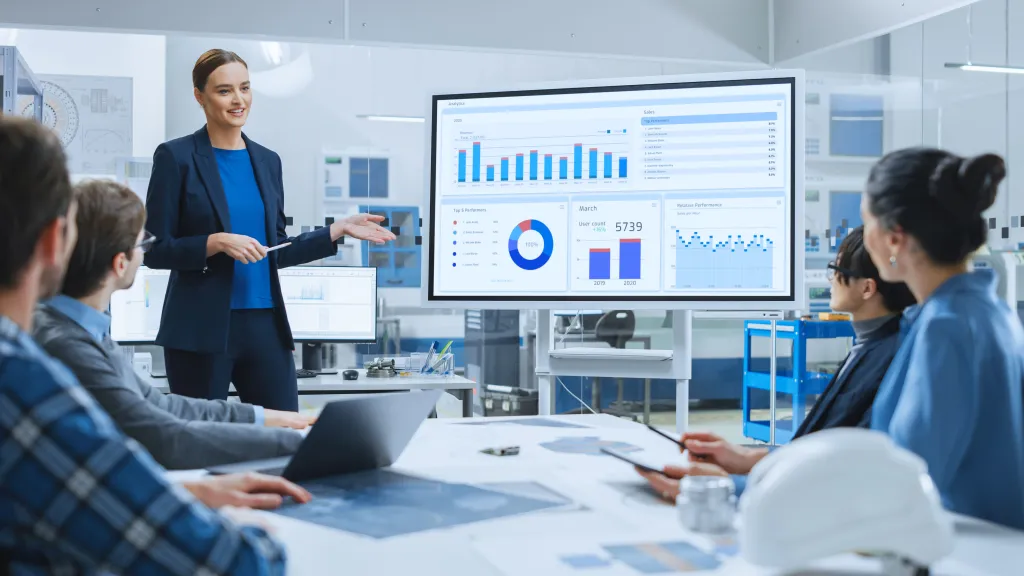 Person in blue jacket presenting data charts to colleagues in modern office meeting room.