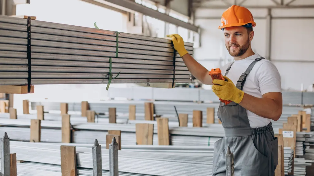 Construction worker in orange helmet reviewing documents in warehouse with stacked building materials.