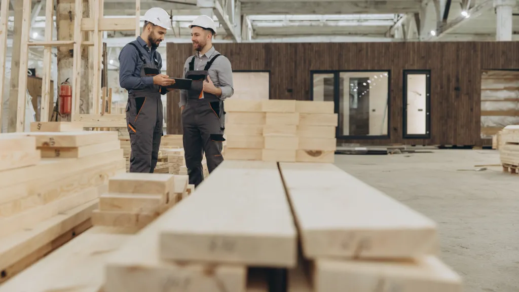 Two people examining lumber in a woodworking workshop or construction site.