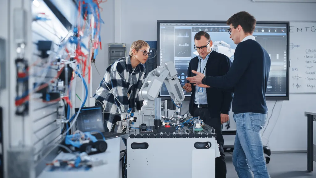 Three people examining robotic equipment in a bright laboratory setting.
