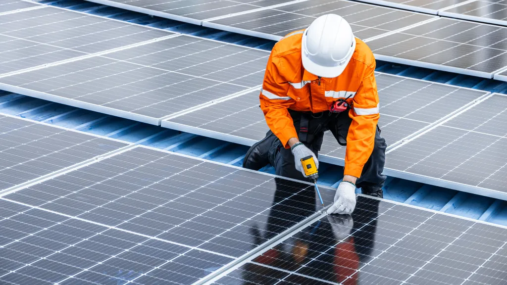 Technician in orange safety gear installing solar panels on rooftop.