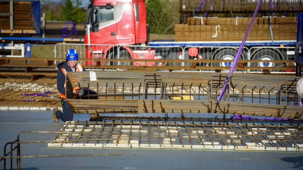 Construction workers on a bridge project with red truck visible in the background.