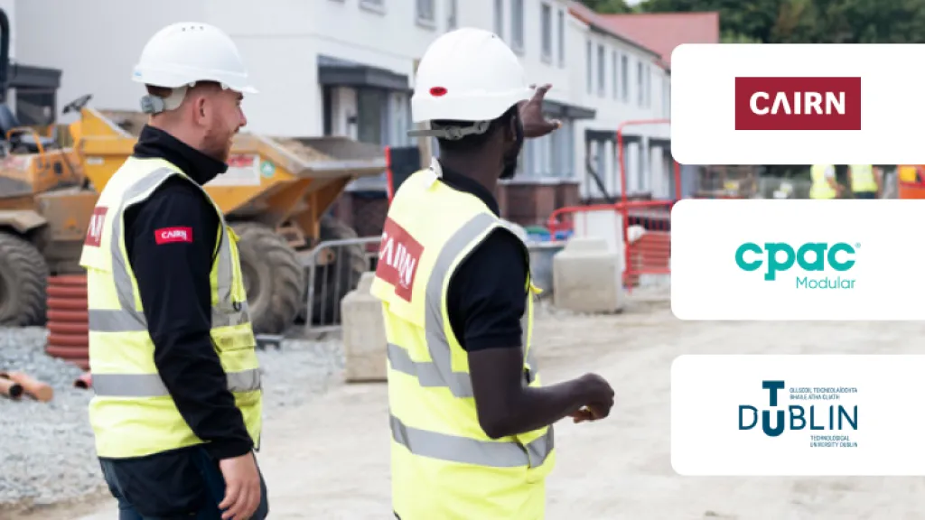 Two construction workers in safety vests and hard hats at a building site, with company logos visible.