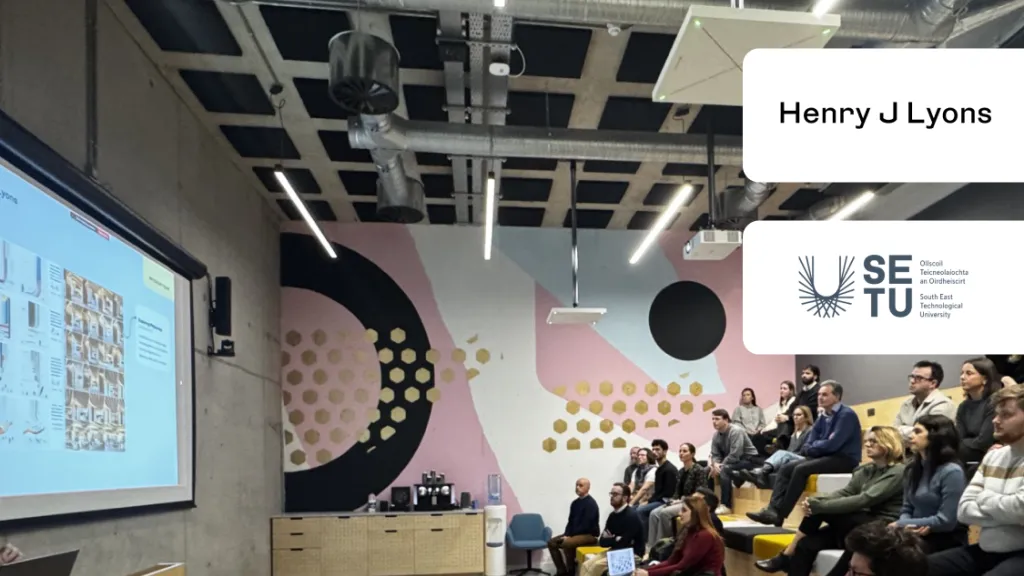 Audience seated in a modern lecture hall with geometric wall designs and digital screens.