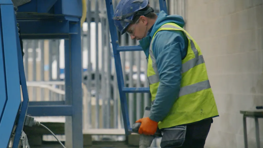 Worker in yellow safety vest and blue hard hat operating industrial equipment.