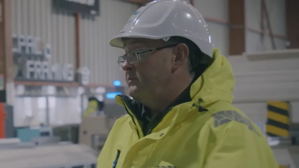 Man in yellow jacket and white hard hat in an industrial warehouse setting.