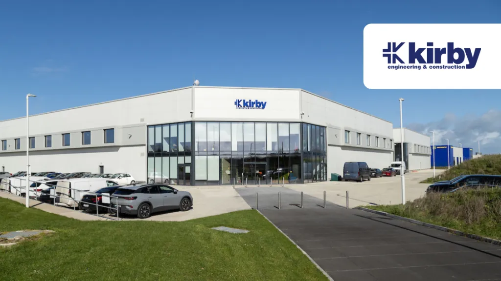 Large modern Kirby industrial building with parked cars outside under a partly cloudy sky.