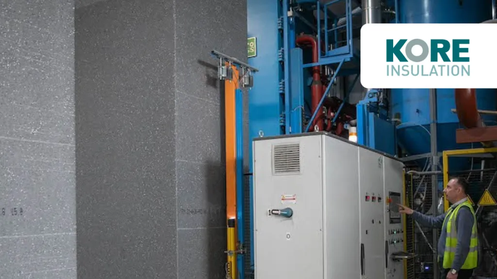 Industrial facility with large insulated panels and blue machinery, worker in safety vest visible, KORE Insulation logo.