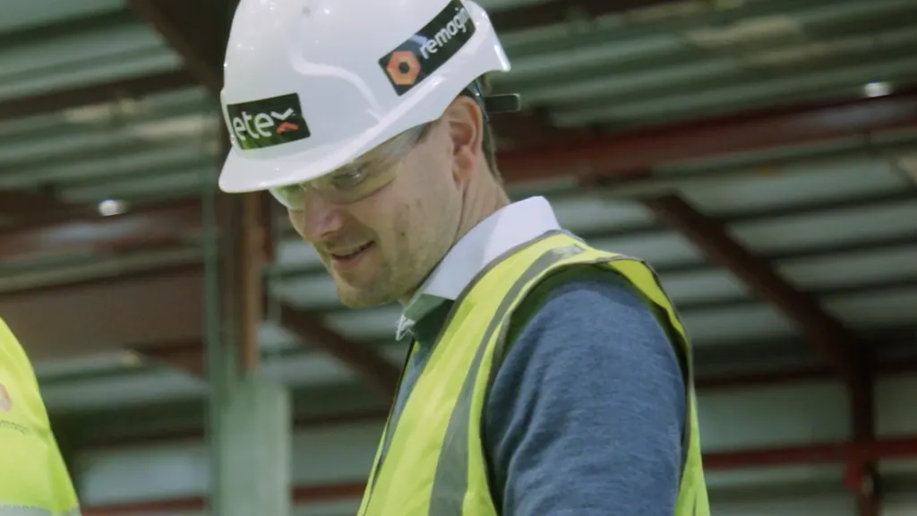 Man in white hard hat and yellow safety vest reviewing documents at a construction site.