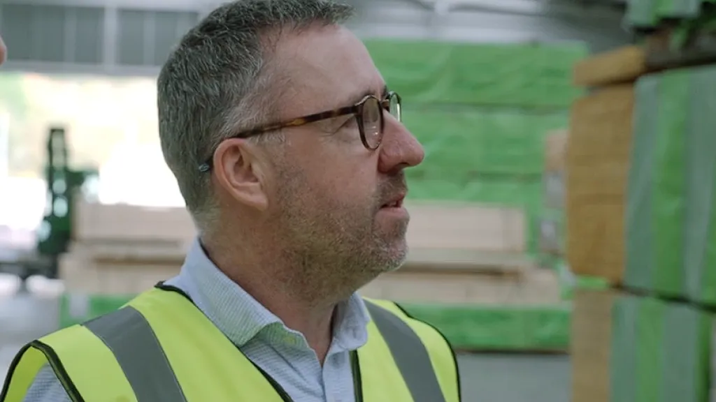 Man in yellow safety vest standing near stacked green insulation materials in a warehouse.