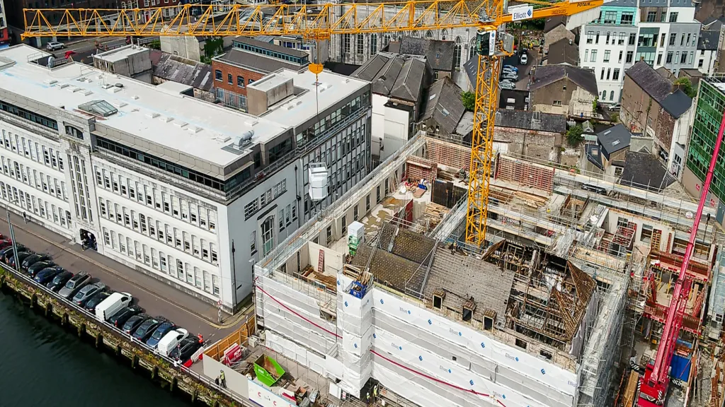 Aerial view of an active urban construction site with yellow cranes beside a waterfront.