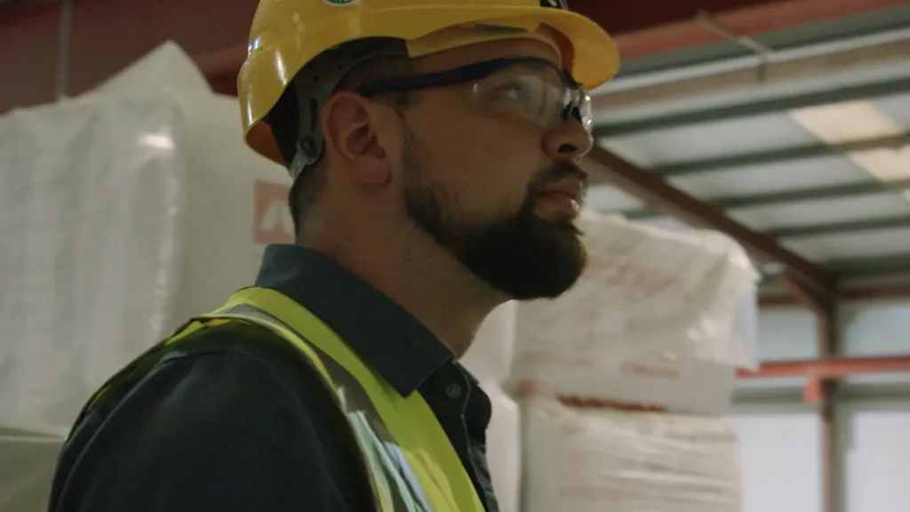 Man wearing a yellow hard hat and safety vest in an industrial warehouse setting.