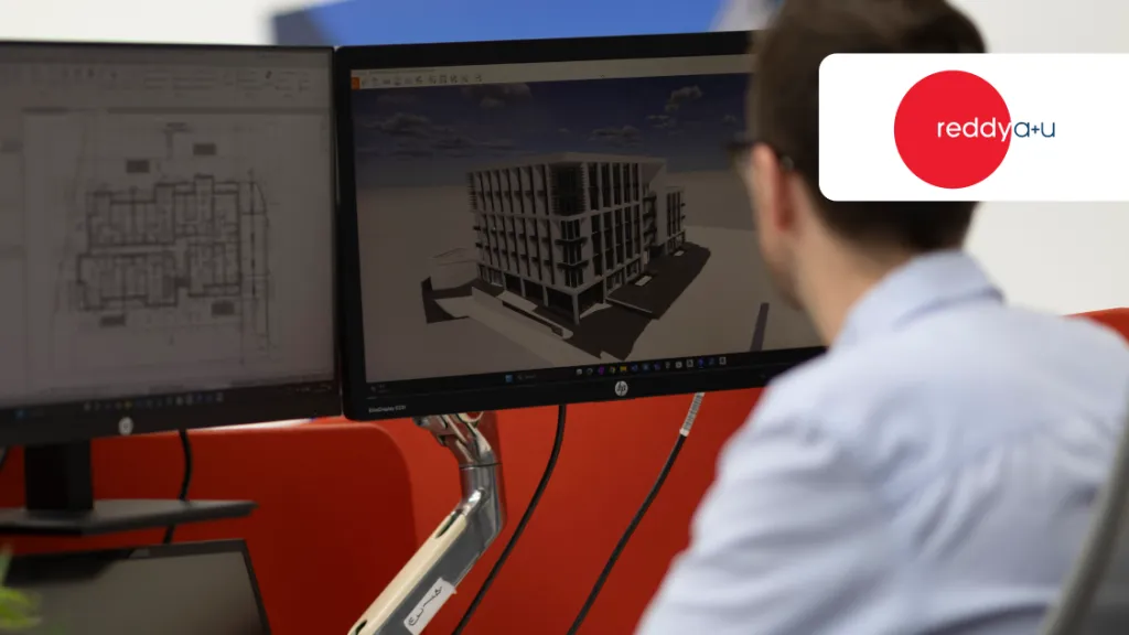 Man working at a computer displaying a 3D architectural building model in CAD software.