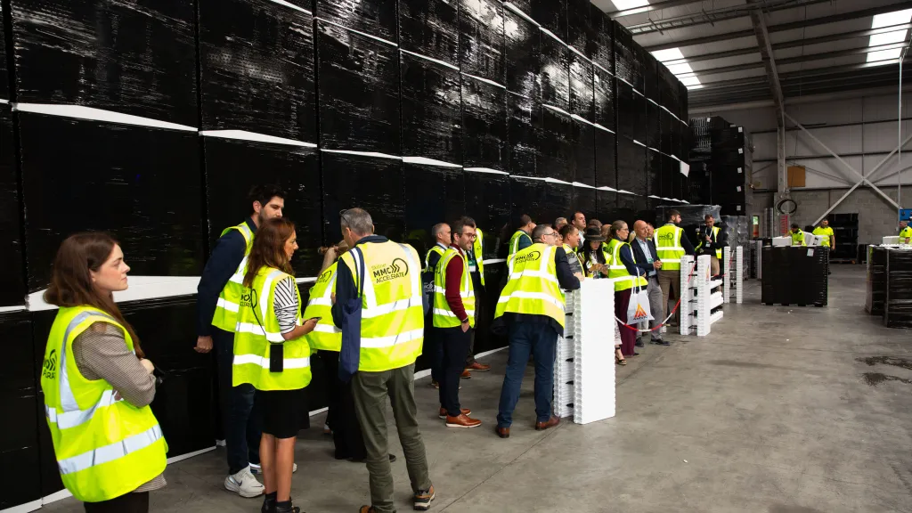 Group of visitors in yellow safety vests touring a large industrial facility.