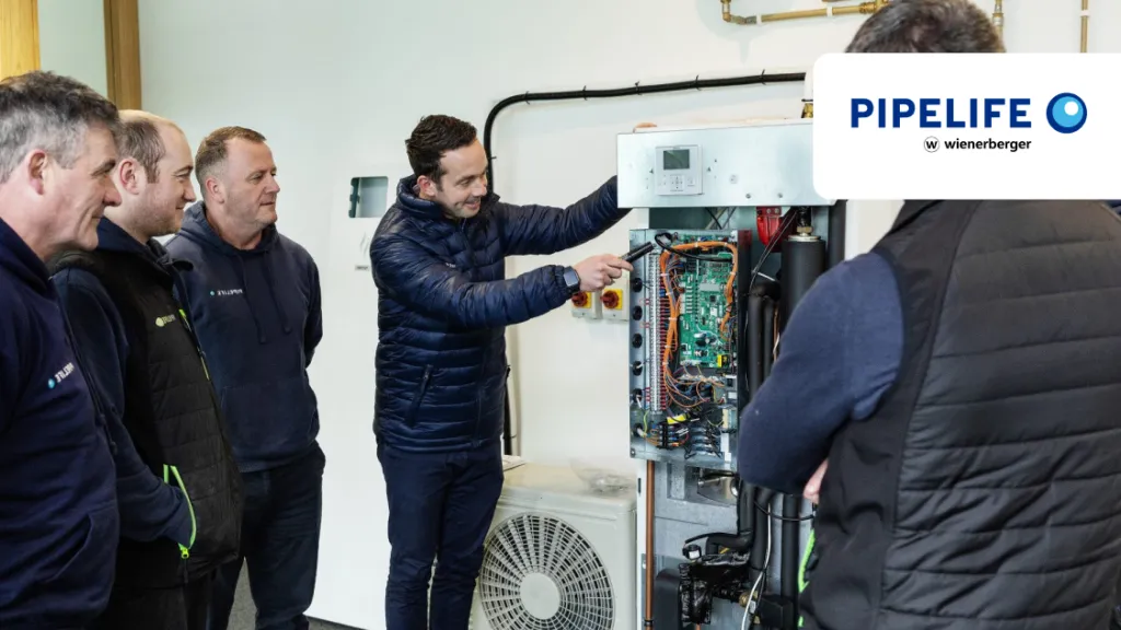 Three men examining an open heat pump unit during a Pipelife training session.