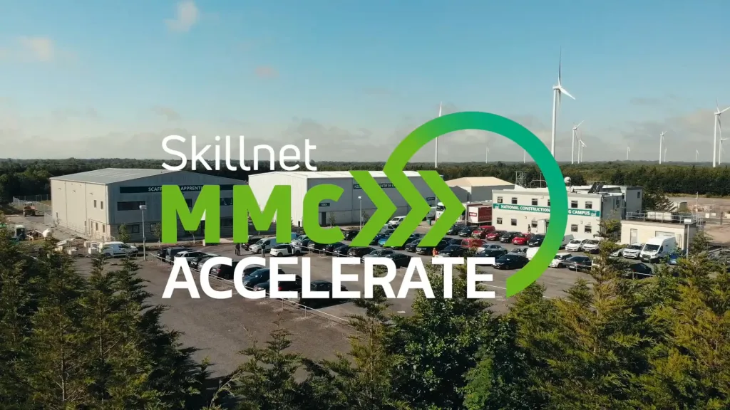 Skillnet MMC Accelerate logo overlaid on an aerial view of a modern industrial facility with wind turbines.