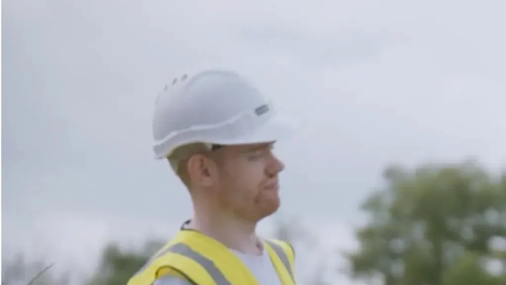 Man in white hard hat and yellow high-visibility vest at an outdoor construction site.