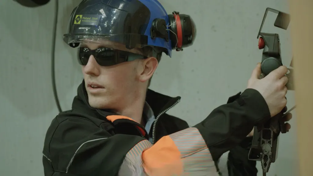 Person wearing sunglasses and ear protection, aiming a pistol in a shooting range.