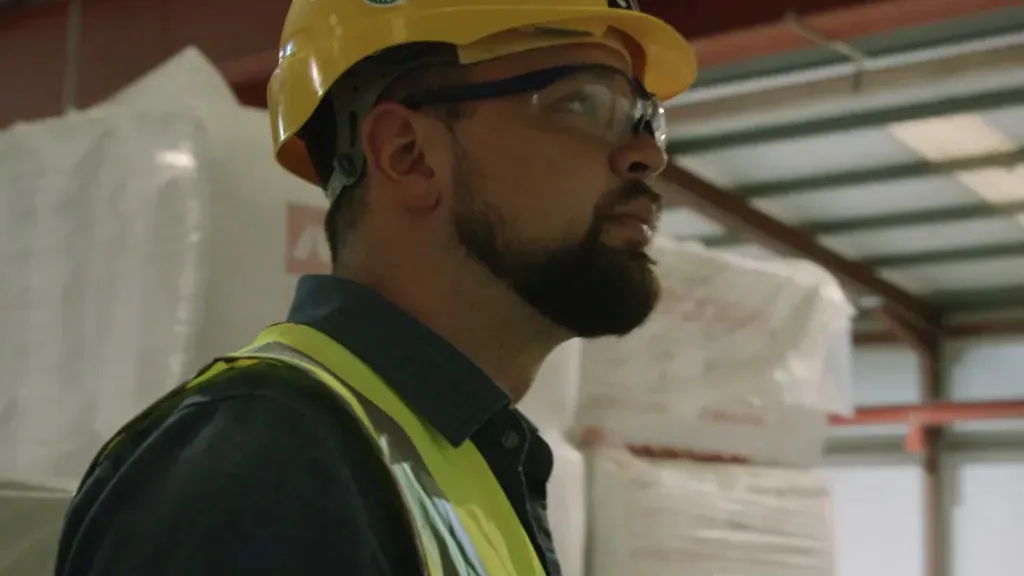 Man wearing a yellow hard hat and safety vest in an industrial warehouse setting.