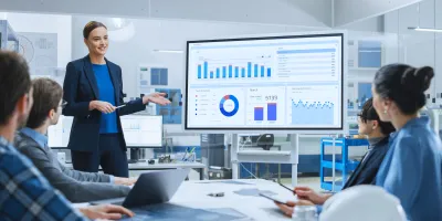 Person in blue jacket presenting data charts to colleagues in modern office meeting room.