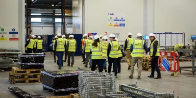 Group of workers in yellow safety vests touring a large industrial warehouse facility.