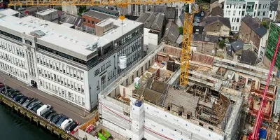 Aerial view of an active urban construction site with yellow cranes beside a waterfront.