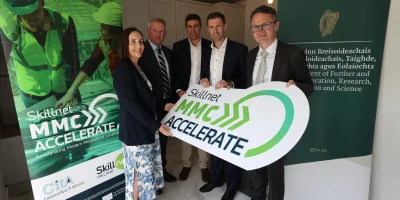 Five professionals posing together, holding a green "MMC Accelerate" sign at a formal event.