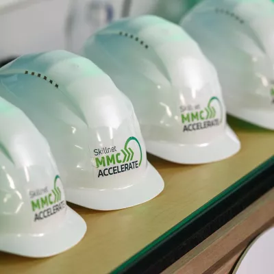 White hard hats are placed on the table, featuring the Skillnet MMC Accelerate logo.