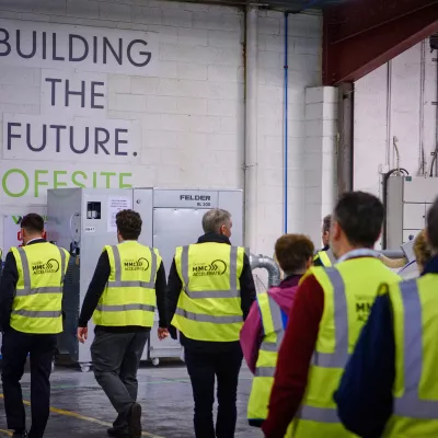 A group of people in high vis vests walk through a white brick corridor.