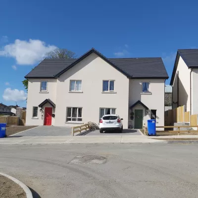 Two modern white semi-detached houses with a white car parked in the driveway.