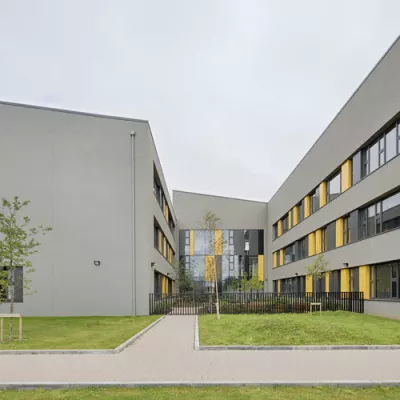Modern grey school buildings, fronted by green lawns