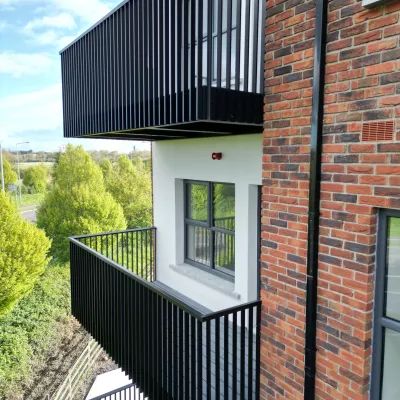 Two modern black metal balconies on a white and brick-finish apartment building.