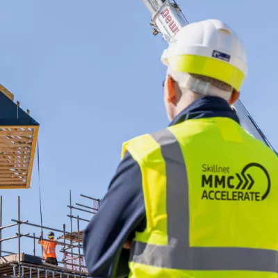 Person wearing a hard hat and high-vis vest looking at a construction site.