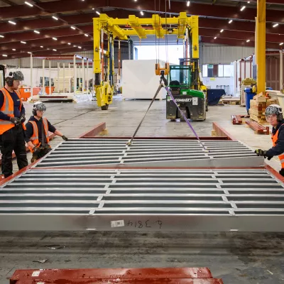 Three people in high vis vests inspect metal frames lying on the ground.