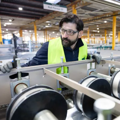 A male with protective goggles and gloves observes a silver machine at work.