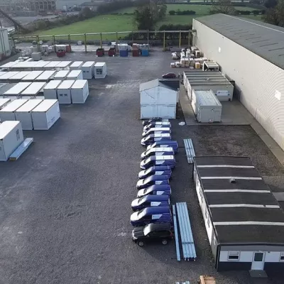 Row of modular building units and rows of vans on either side of a car park.