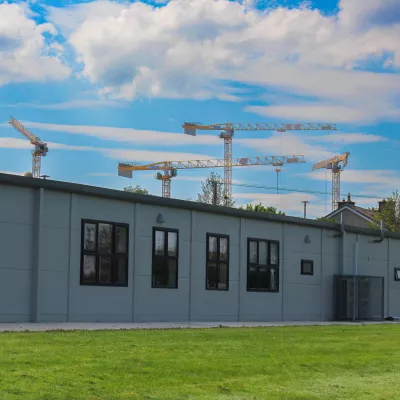 Modern grey school buildings with four large yellow cranes in the background.