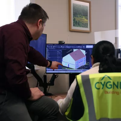 Two people in an office reviewing a 3D building model on a computer screen