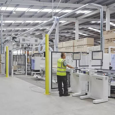 Person in high-vis vest operating a robotic system inside a construction manufacturing facility.