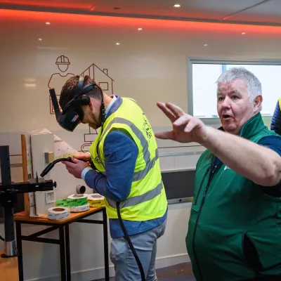image of 2 men, one is holding a welder in a high vis jacket and the other is gesturing offscreen