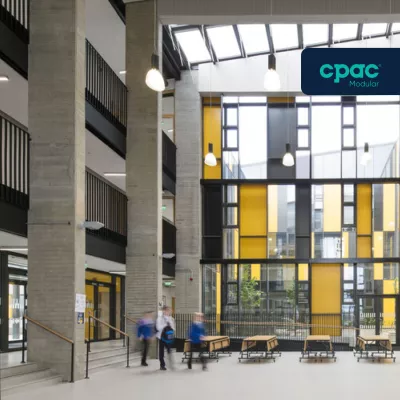 Glass atrium space in a modern school building, with three blurred students passing.