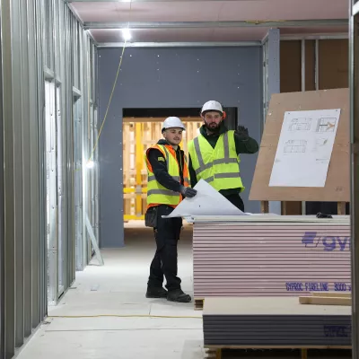 Two people in high-vis vests and hard hats reviewing plans inside a construction unit.