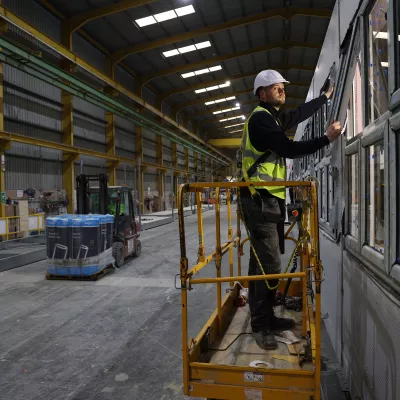 A male in a hard hat and high vis vest stands on a yellow scissor lift to test a window.