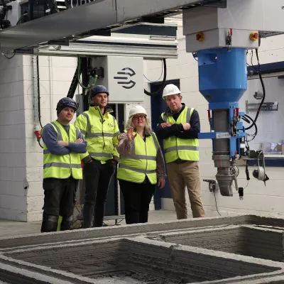 men standing for a photo in high vis jackets in front of a 3d house printing machine