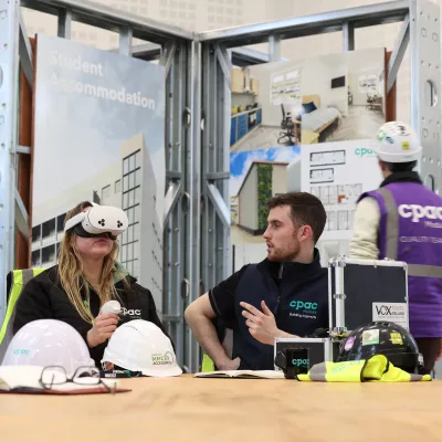 Two people sitting at a table, with the male watching as the female uses a VR headset.