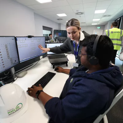 Two people are at a workstation, one is showing construction drawings on the screen to the other.