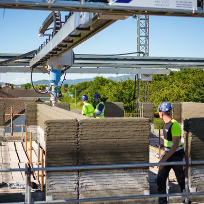 Workers operating a 3D concrete printing machine on a сonstruction site.