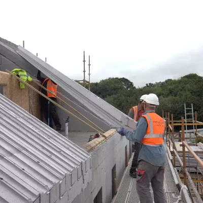 A group of three people in high vis jackets and hard hats working to construct the roof of a house.