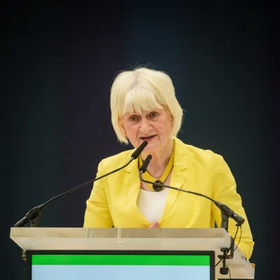 A person wearing a yellow blazer speaking at a podium.